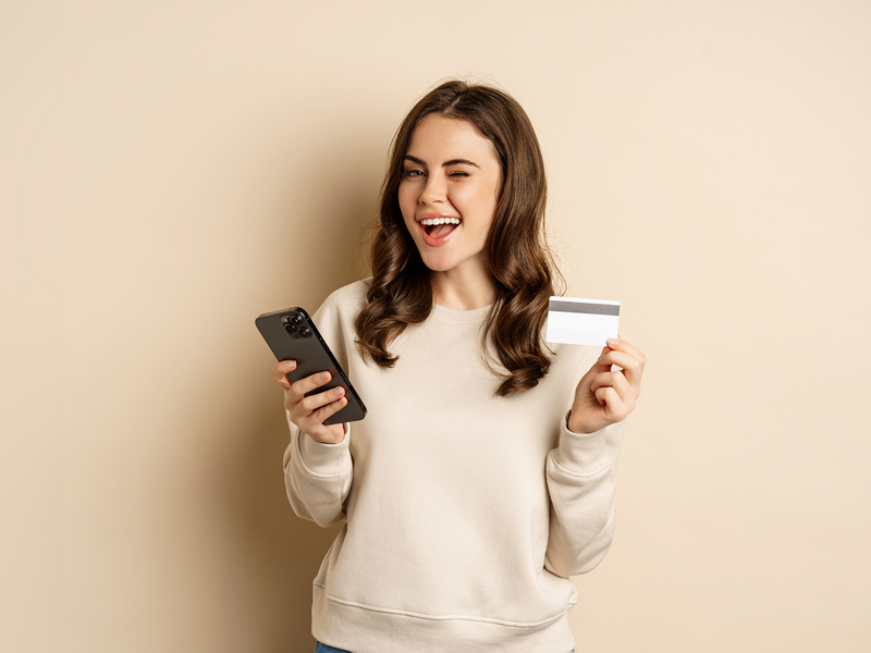 Tânără ținând un card și un telefon, ilustrând serviciile PlusCredit pentru credite de nevoi personale.